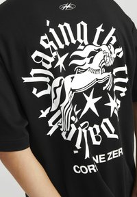 Sort T-shirt med et stort hvidt grafik af en oprejst hest, omgivet af stjerner og fed tekst, med rund halsudskæring og korte ærmer.