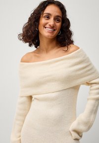 Off-shoulder crèmekleurige ribgebreide trui met lange mouwen, met een getailleerd silhouet en een zachte textuur.