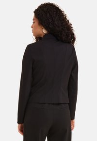 Blazer nero su misura con un design aderente, spalle strutturate e una texture del tessuto liscia. Retro leggermente accorciato con dettagli di cucitura.