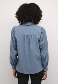 Blauwe chambray overhemd met een achterpaneel, geplooide details en lange bolle mouwen. Beschikt over knoopmanchetten en een afgeronde zoom.