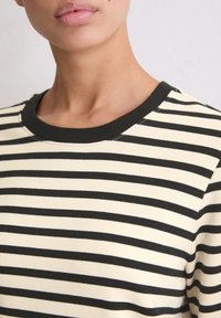 Gestreepte langetermijnshirt in crème en zwart. Zachte stof, ontwerp met ronde hals, met gelijkmatig verdeelde horizontale strepen en een effen zwarte halslijn.