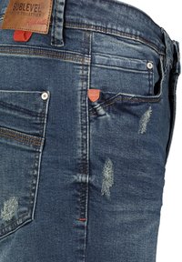 Donkerblauwe denim jeans met vervaging, versleten accenten, vijf zakken, een bruine leren merklabel en rode stiksel op de tailleband.