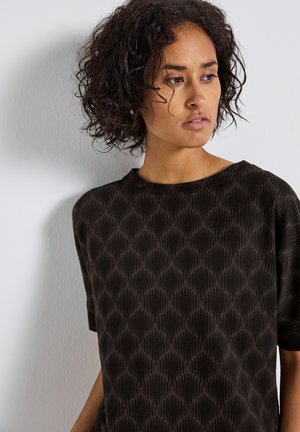 Un haut noir ample avec un motif texturé en gris foncé, un col rond et des manches courtes, sur un fond neutre.