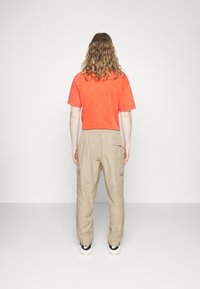 Röd t-shirt med kort ärm och beige cargobyxor. Byxorna har sidofickor. Bärs med svarta och vita sneakers. Enkel design med avslappnad passform.