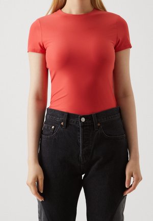 Roter Kurzarm-Body aus dehnbarem Stoff, figurbetont, kombiniert mit hochtaillierten schwarzen Jeans mit Fronttaschen und silbernen Beschlägen.