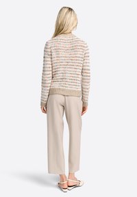 Pull en maille crème avec des flecks multicolores, doté d'une base et d'un col côtelés, assorti à un pantalon beige clair et des chaussures claires.