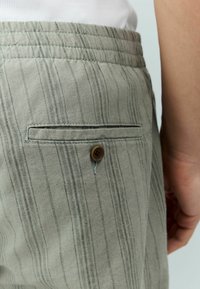 Szare w paski spodnie wykonane z teksturowanej tkaniny, z zapinaną na guzik tylną kieszenią oraz pikowanym pasem w celu dodania detali.