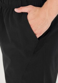 Svarta träningbyxor med elastisk midja, med en sidoficka, slät textur och ett andningsbart nätinslag nära fickan.