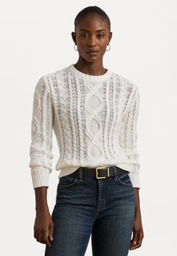 Sweater branco de malha com um design texturizado de cabos, decote redondo e punhos canelados. Combinado com jeans escuros e um cinto preto.