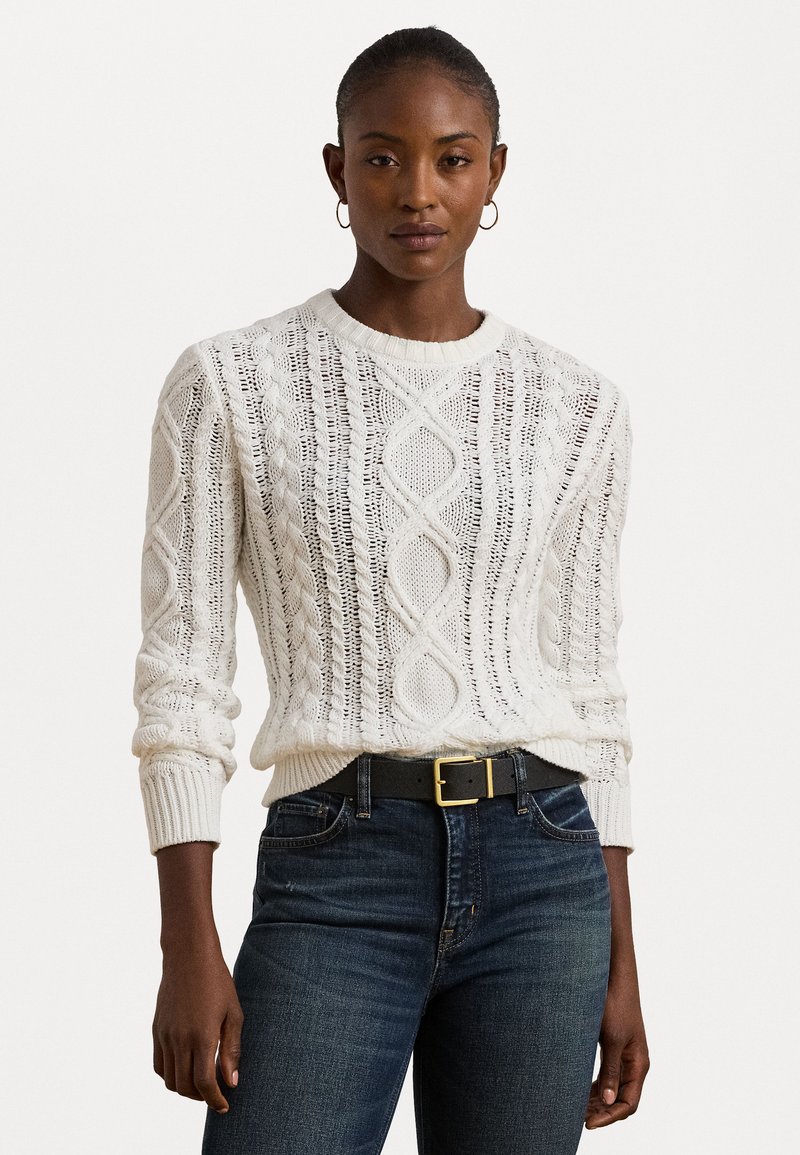 Sweater branco de malha com um design texturizado de cabos, decote redondo e punhos canelados. Combinado com jeans escuros e um cinto preto.