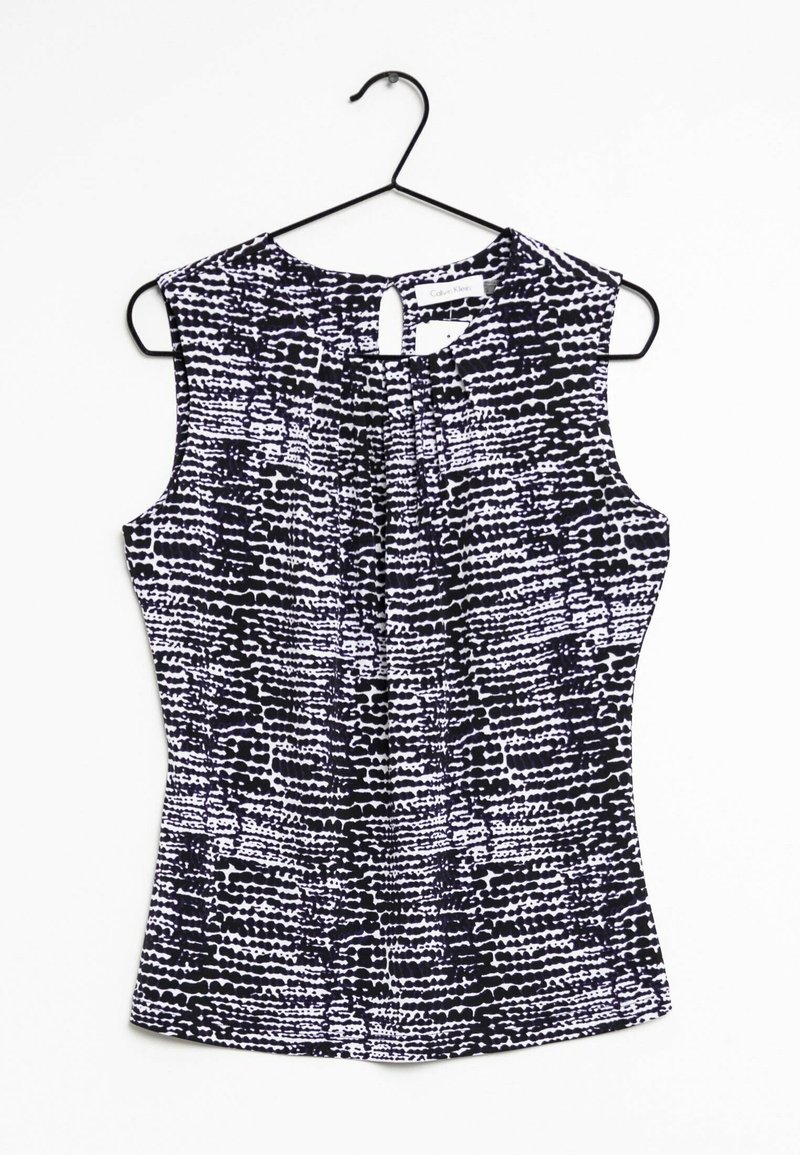 Haut sans manches pour femme à motif noir et blanc avec un pli devant, suspendu sur un cintre noir sur fond blanc.