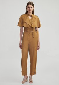 Mosterdgele twee-delige outfit met een cropped top met cape-ontwerp en wijde broek met zakken en strikdetails.