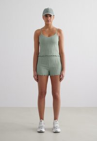 Débardeur côtelé vert clair, court, avec des bords festonnés, accompagné de shorts assortis. Porté avec une casquette de baseball vert clair et des baskets blanches.