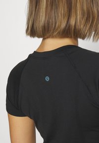 Zwart atletisch shirt met een ronde halslijn en korte mouwen, gemaakt van een gestructureerde stof en met een klein blauw logo op de achterkant.