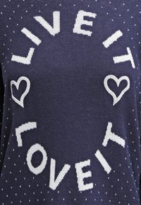 Mörkblå tröja med vit text "LEVA DET ÄLSKA DET" prydd med små hjärtsymboler och en strukturerad stickad mönster.