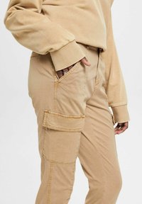 Beiga cargobyxor med rak ben-design, som har sidfickor, synlig sömnad och en mjuk bomullstextur.