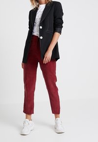 Blazer noir avec couture blanche et deux boutons, associé à un pantalon en velours côtelé bordeaux et des baskets blanches. Tenue décontractée avec des couleurs contrastées.
