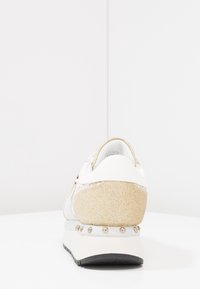 Hvide sneakers med en tekstureret guldglitter hæl, lysegrå detaljer og dekorative metalnitter på mellemsålen.