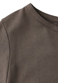 Ruskea puuvillakangas, lähikuva pyöreästä kaula-aukosta, jossa on sileä pinta ja näkyvät ribbistitchaukset reunoilla.