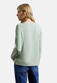 Miętowy sweter z prążkowanym dekoltem i mankietami, miękka tekstura, luźny krój, zestawiony z niebieskimi dżinsami, widok z tyłu.
