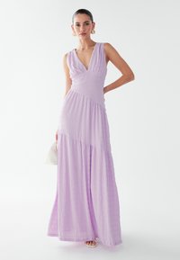 Lavender maxi dress with a v-neck, gathered bodice, and textured fabric. Features a flowing skirt and a fitted waistline.