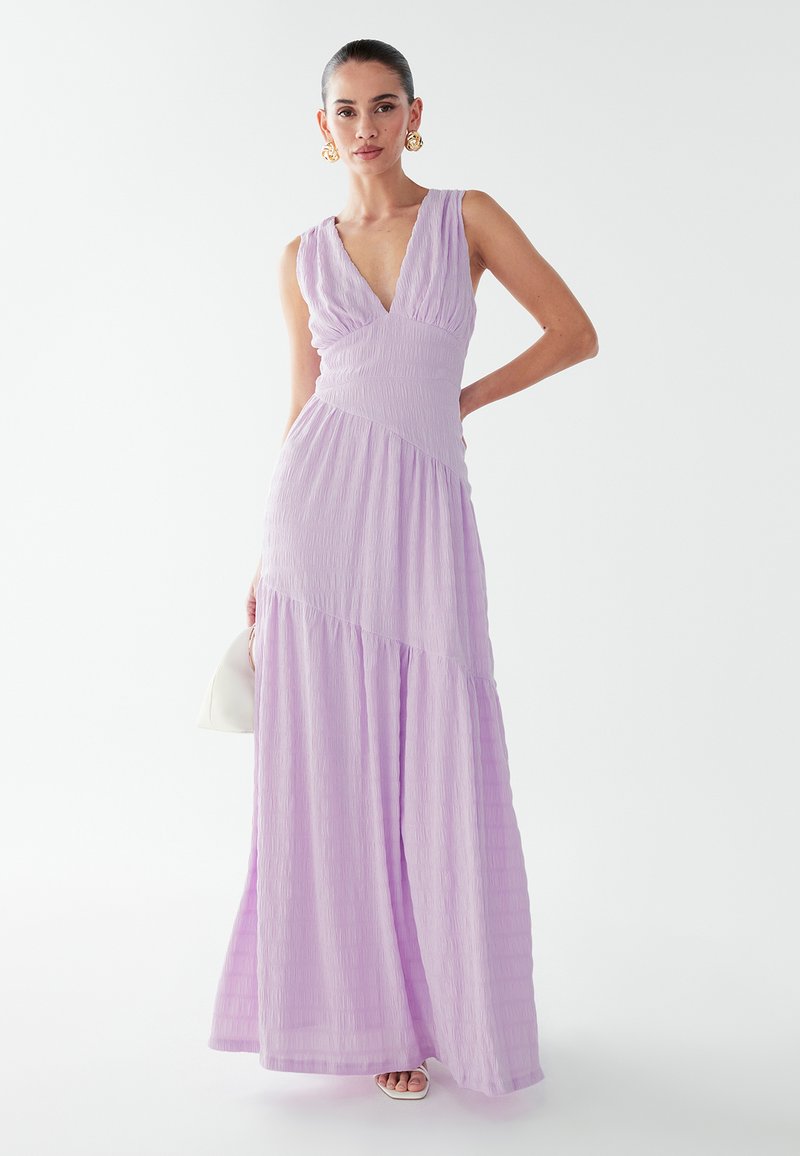 Lavender maxi dress with a v-neck, gathered bodice, and textured fabric. Features a flowing skirt and a fitted waistline.