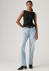 Crna top bez rukava, svijetloplave traperice ravnog kroja, crni remen i crne gležnjače. Glatki materijal i opušteni kroj s minimalnim detaljima.