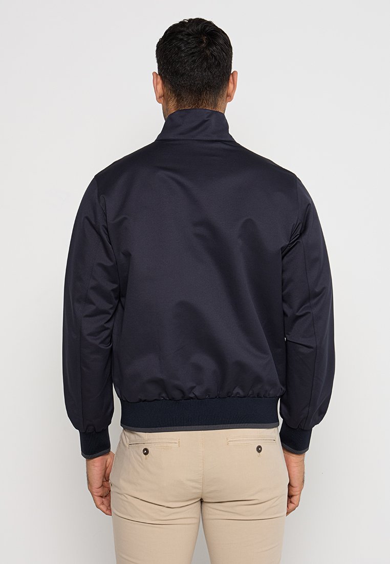 Navyblaue Bomberjacke aus glattem, glänzendem Stoff. Sie verfügt über einen hohen Kragen, elastische Bündchen und einen elastischen Bund sowie ein schlichtes Design.