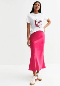 Witte t-shirt met een grafisch ontwerp van een wijnfles en glas, gecombineerd met een gladde, helderroze satijnen rok en witte sneakers met rode accenten.