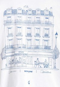 Witte t-shirt met een blauwe lijntekening van een Parijse gebouw met balkons, een café-scène, en de tekst "SIXTH JUNE" en "Sinds 2008."