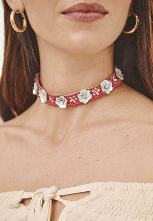 Chocker de tela roja adornado con acentos de flores blancas y rosas, con un acabado texturizado y un diseño simple.