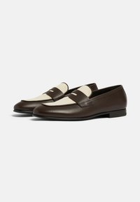 Braune Lederloafers mit beige Farbdetails, einem eleganten Design, flacher Sohle und einem dekorativen Riemen über dem oberen Teil.
