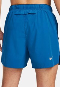 Pantalones cortos deportivos azules hechos de tela ligera, con una cinturilla elástica, una pequeña abertura lateral y un pequeño logo gris en el dobladillo inferior.