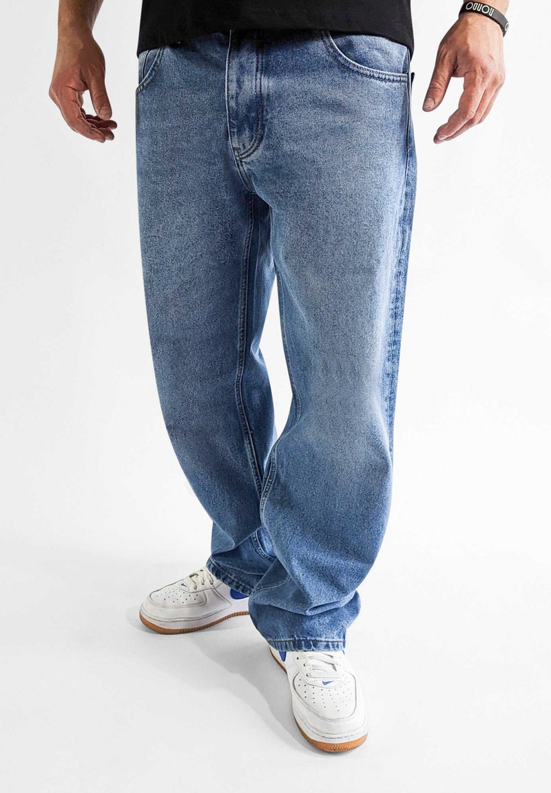 Lyseblå denimjeans med løs passform. Har fem lommer, synlige sømmer og en lett falming. Kombinert med hvite joggesko.
