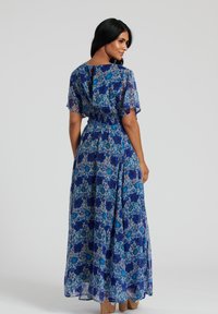 Maxiklänning i blå blommig print med genomskinliga korta ärmar och smockad midja. Har en nyckelhålsdesign på ryggen och en fladdrande siluett.