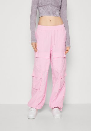 Roze cargobroek met een elastische tailleband, twee zijzakken en een losse pasvorm. Draagt met witte sneakers en een grijs shirt met lange mouwen.