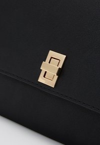 Borsa a tracolla in pelle nera con un elegante chiusura rettangolare in metallo dorato, texture liscia e cuciture precise lungo i bordi.