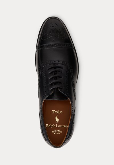 Zapato de vestir Oxford de cuero negro con detalles brogue y cordones, visto desde arriba mostrando la plantilla marrón con la marca Polo Ralph Lauren.