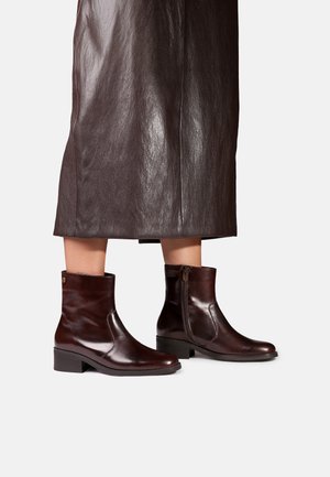 Bottines en cuir brun foncé brillant à talons blocs bas portées avec une jupe en cuir brun foncé assortie.