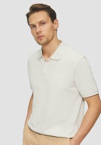 Licht crèmekleurig poloshirt van zachte stof, met een kraag en drie knopen. Subtiele logo-detail op de borst.