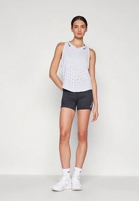 Baltas rankovių sportinis marškinėlis su perforuotu dizainu, derinamas su juodais šortais ir baltais sportbačiais. Paprastas, sportiškas išvaizda.