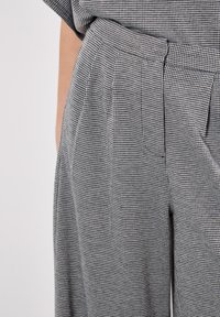 Svart och vit houndstooth-mönstrad byxa med hög midja, plisserad front och sidfickor, gjord av lättviktsmaterial.