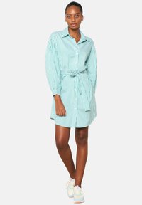 Abito camicia a righe blu chiaro e bianco, con maniche lunghe, cintura in vita e una vestibilità rilassata. Abbinato a sneakers sportive.