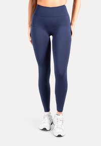 Marineblauwe leggings met hoge taille en zijzak; gladde textuur, elastische tailleband en aangesloten pasvorm, gecombineerd met witte sportschoenen.