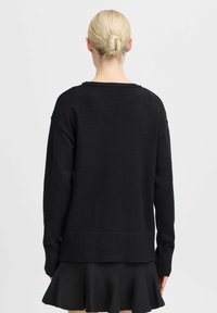 Pull en tricot noir à coupe décontractée, avec des poignets côtelés et un ourlet arrière légèrement plus long, doté d'un col rond et d'une texture lisse.