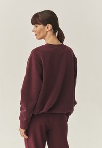 Bordeaux oversized sweatshirt gemaakt van zacht materiaal, met een ronde hals en ribgebreide manchet. Draag het met bijpassende broek.