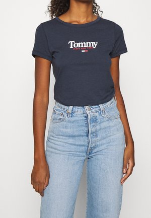 Námořnicky modré tričko s krátkým rukávem a logem "Tommy Jeans New York" v bílé a červené barvě na přední straně. Kombinováno s světle modrými džíny s vysokým pasem.