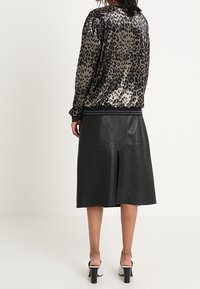 Mikina z sametového materiálu se zvířecím potiskem v šedé a černé barvě, spárovaná s černou koženou midi sukní se zadním rozparkem, oblečená s botami na chunky podpatku.