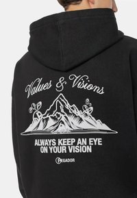 Schwarzer Kapuzenpullover mit einer großen weißen Grafik, die Berge und den Text: "Werte & Visionen" und "Behalte immer deine Vision im Auge" zeigt.