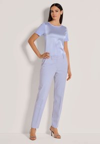 Hellblau satinierte Bluse mit kurzen Ärmeln, kombiniert mit maßgeschneiderten hellblauen Hosen. Das Outfit zeichnet sich durch ein elegantes Design und eine taillierte Silhouette aus.